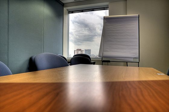 Leerer Besprechungsraum mit Holztisch, blauen Stühlen und Flipchart vor dem Fenster