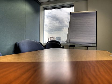 Empty meeting room with wooden table, blue chairs and a flip chart by the window