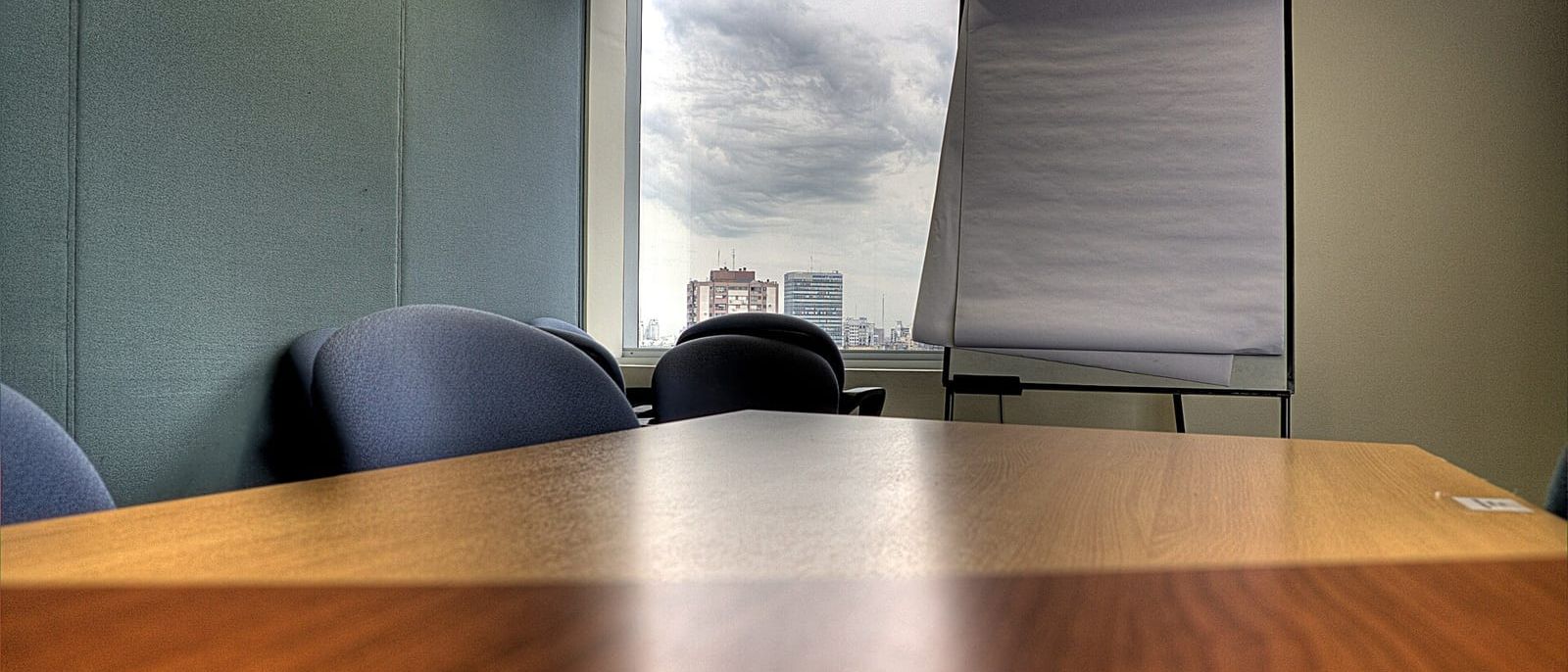 Empty meeting room with wooden table, blue chairs and a flip chart by the window