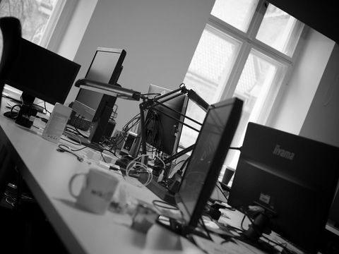 Black-and-white office with several monitors, cables and coffee mugs on a long desk
