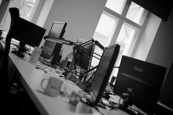 Black-and-white office with several monitors, cables and coffee mugs on a long desk