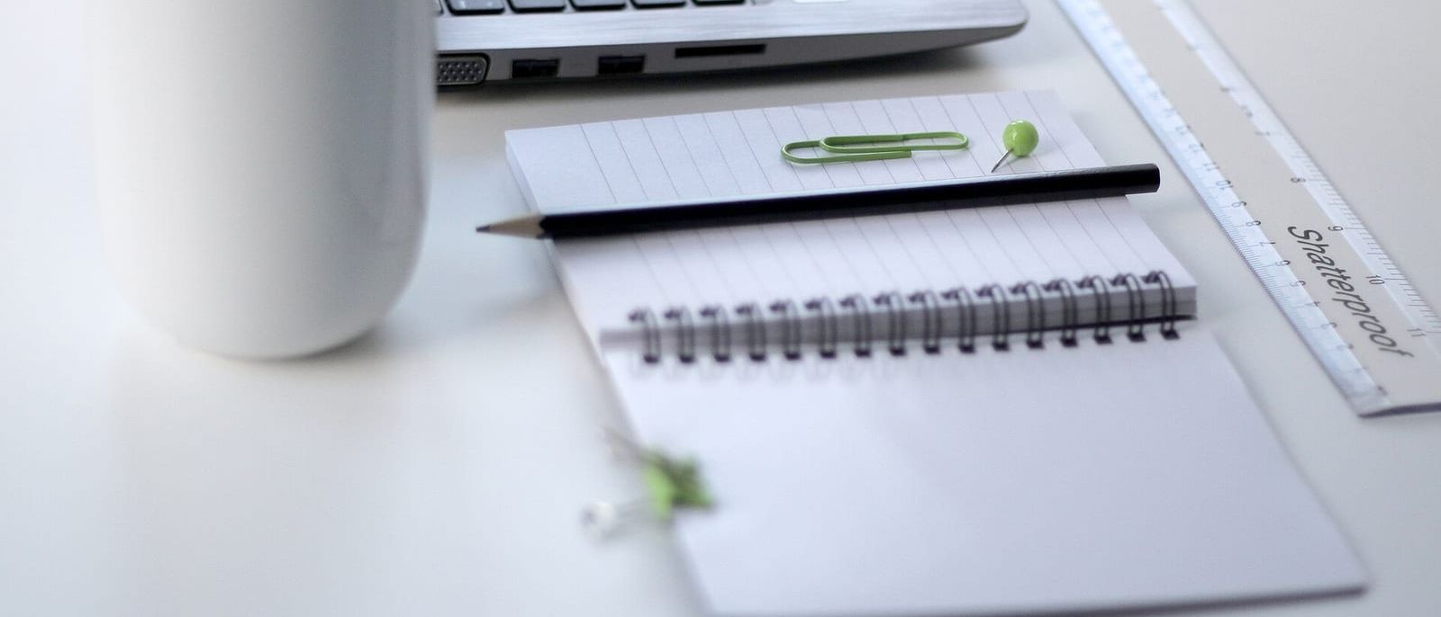 Laptop, weiße Tasse, Spiralblock mit Bleistift und Lineal auf hellem Schreibtisch