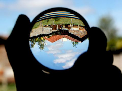 Hand hält eine Lupe, durch die Haus und Himmel kopfüber erscheinen