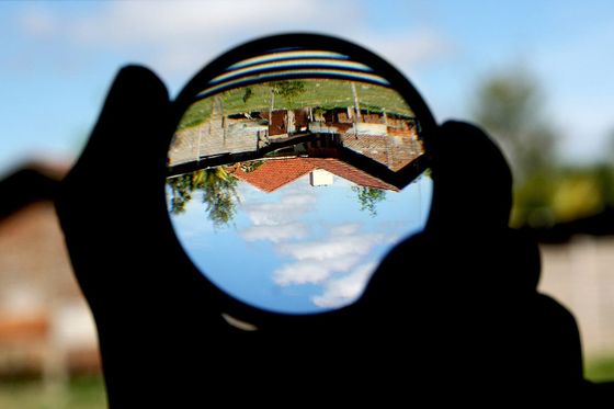 Hand holding a lens that shows a house and sky upside down