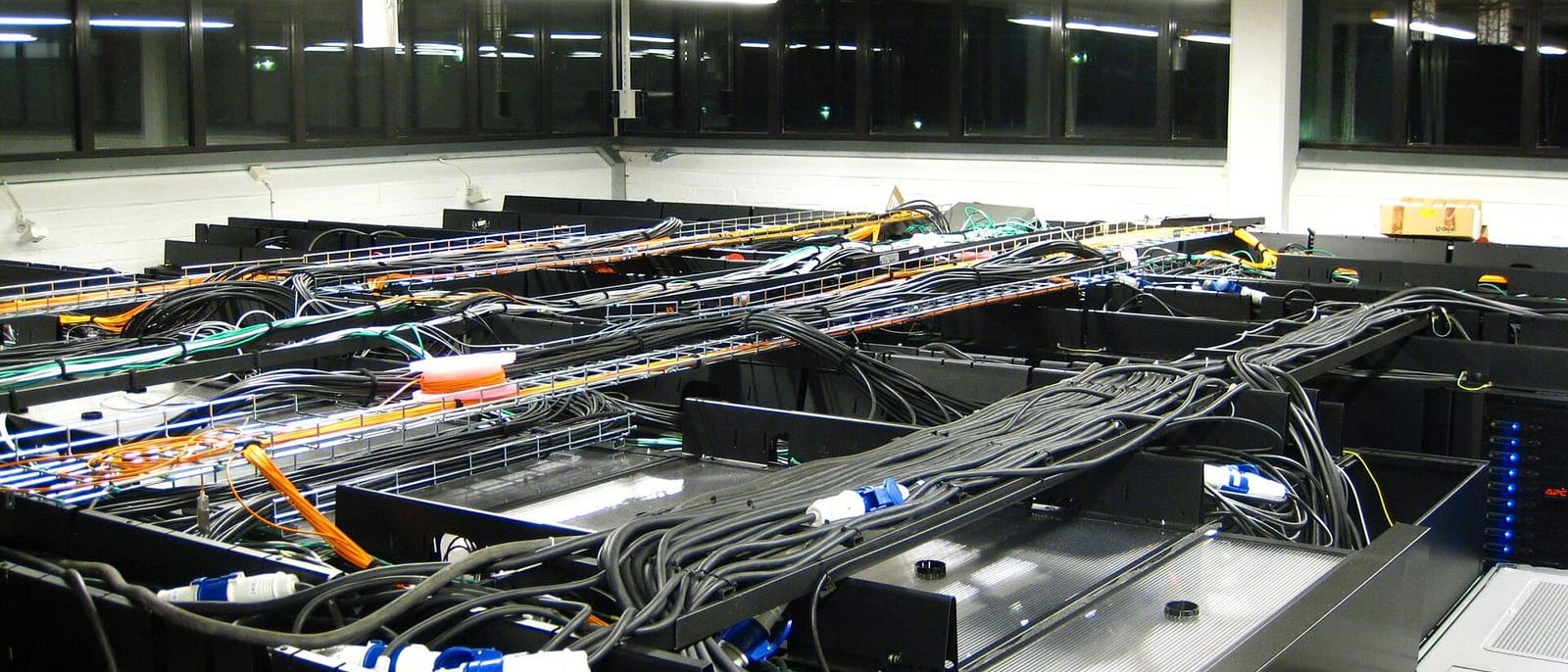 Server room with rows of black racks, cable trays and bundled power cables