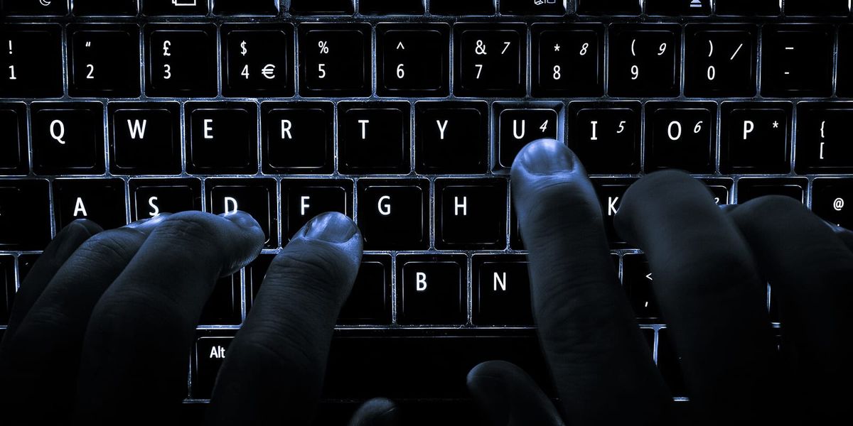 Fingers typing on a backlit laptop keyboard in the dark