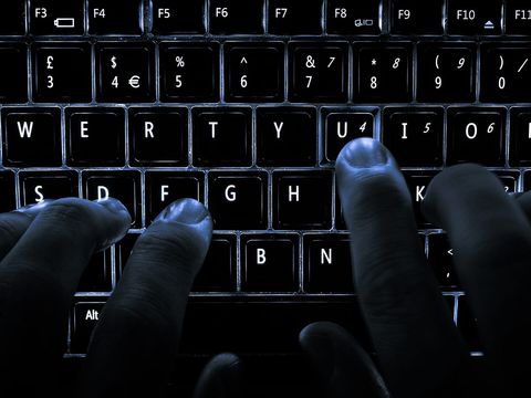 Fingers typing on a backlit laptop keyboard in the dark