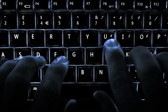 Fingers typing on a backlit laptop keyboard in the dark