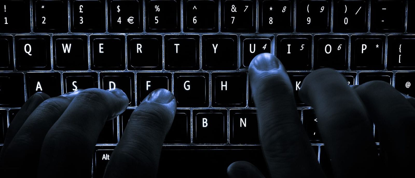 Finger tippen im Dunkeln auf einer beleuchteten Laptop-Tastatur