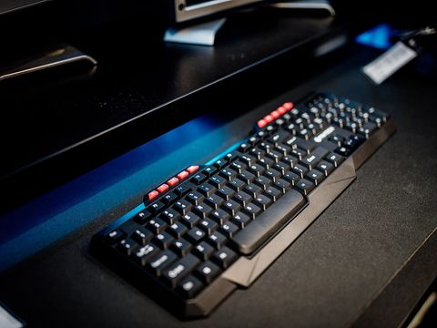Black computer keyboard on a dark desk with monitor stands behind it in blue light