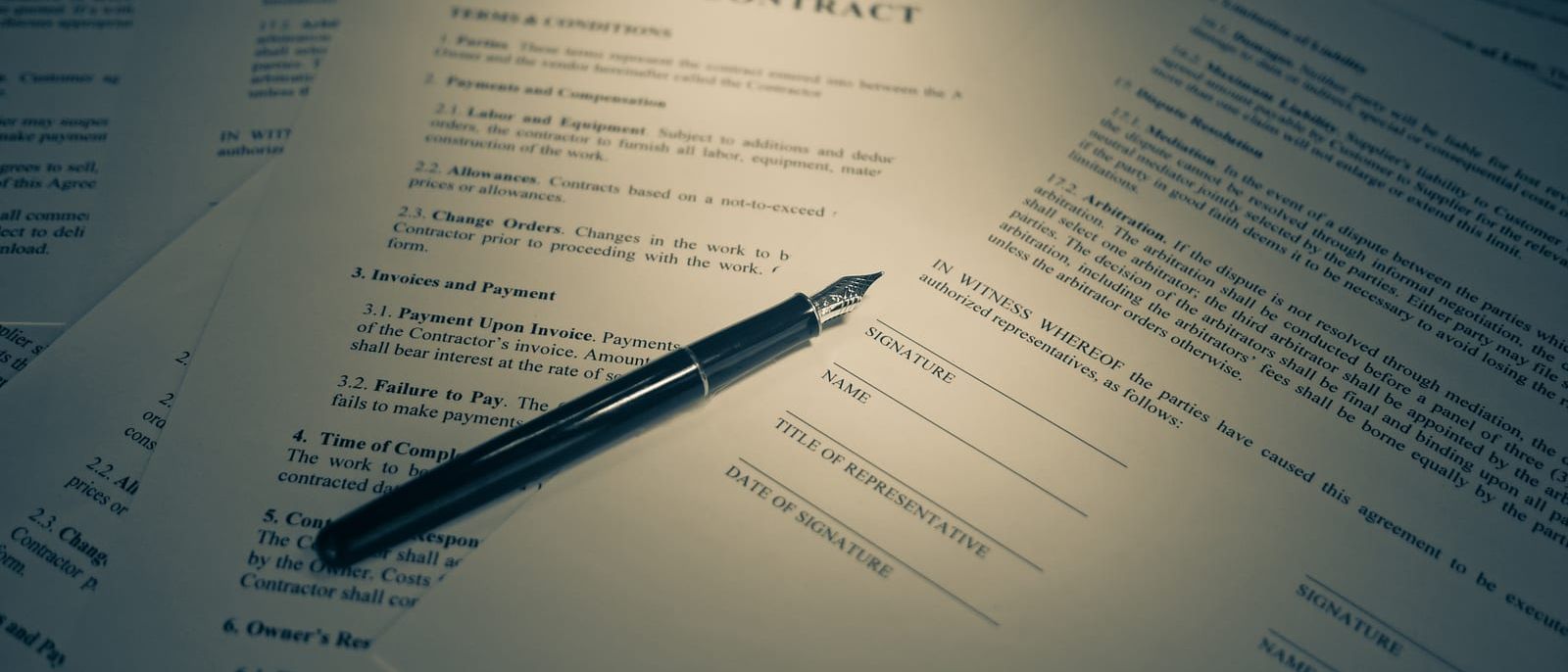 Printed contract with signature lines and a fountain pen lying across it
